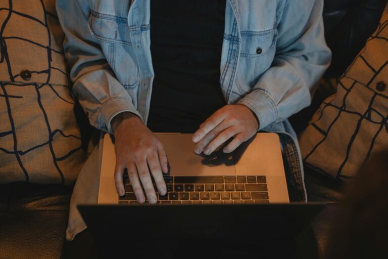 A close-up view of a person typing on a laptop, seated comfortably indoors.